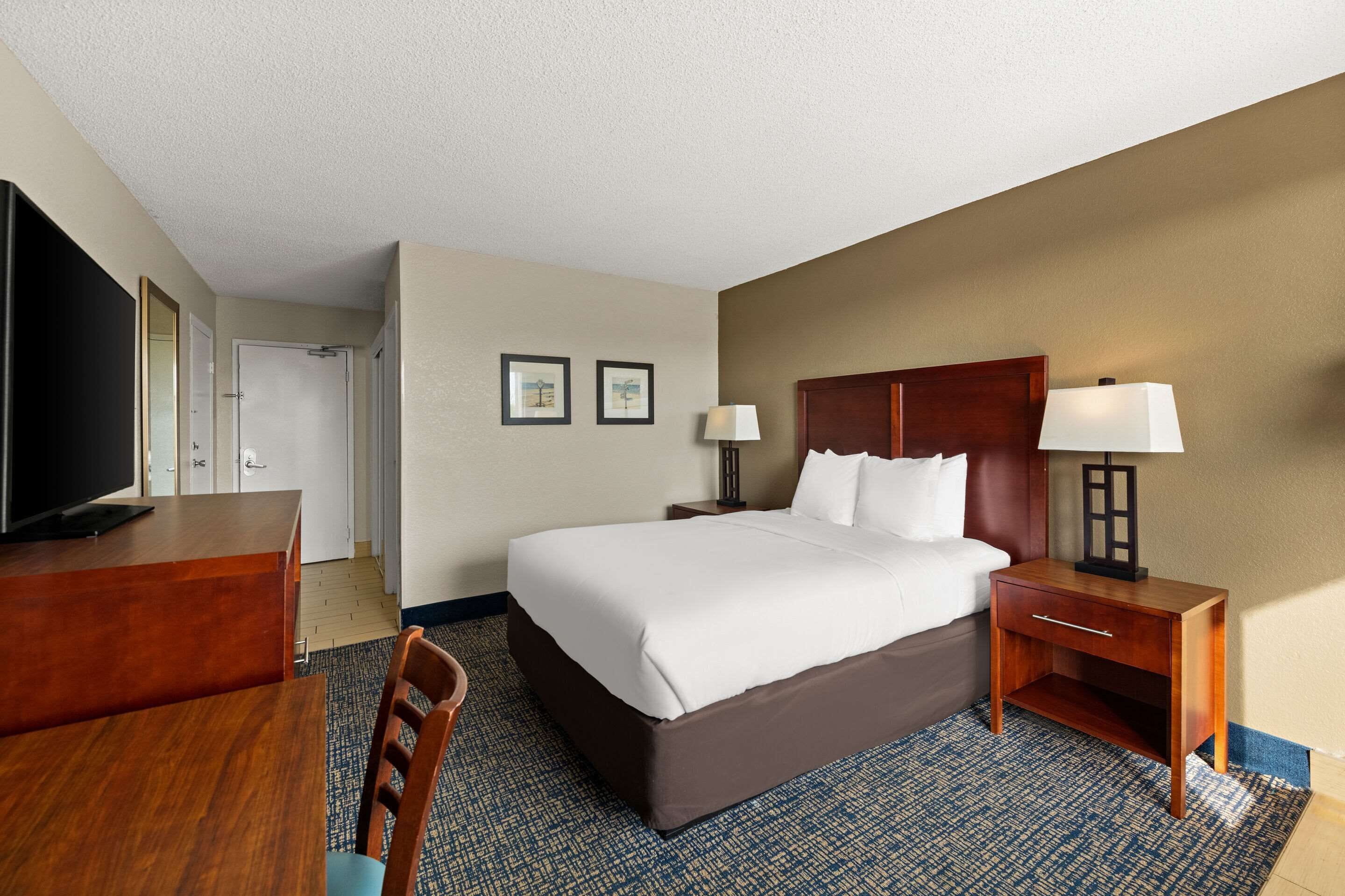 A hotel room with a large bed, a desk, a chair, a TV, and two bedside lamps.