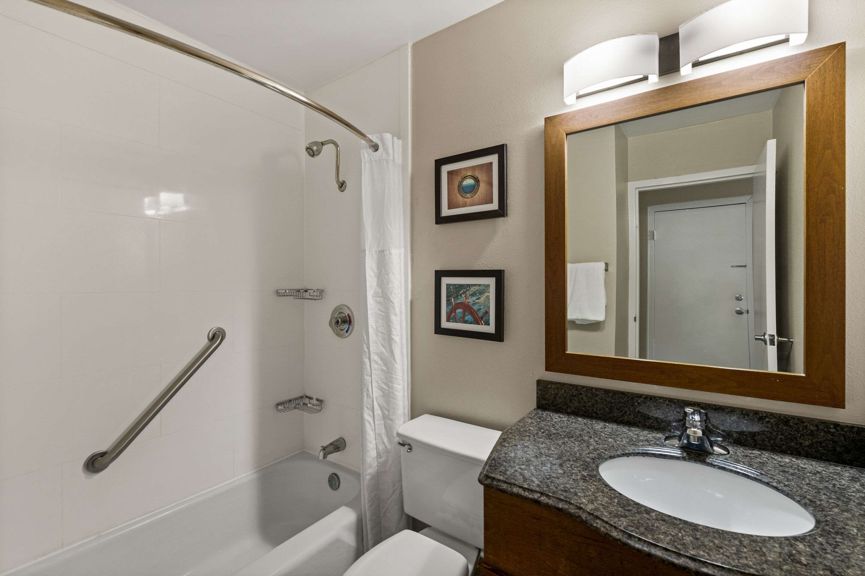 A bathroom with a shower, toilet, sink, and a large mirror.