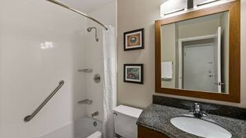 A bathroom with a shower, toilet, sink, and a large mirror.