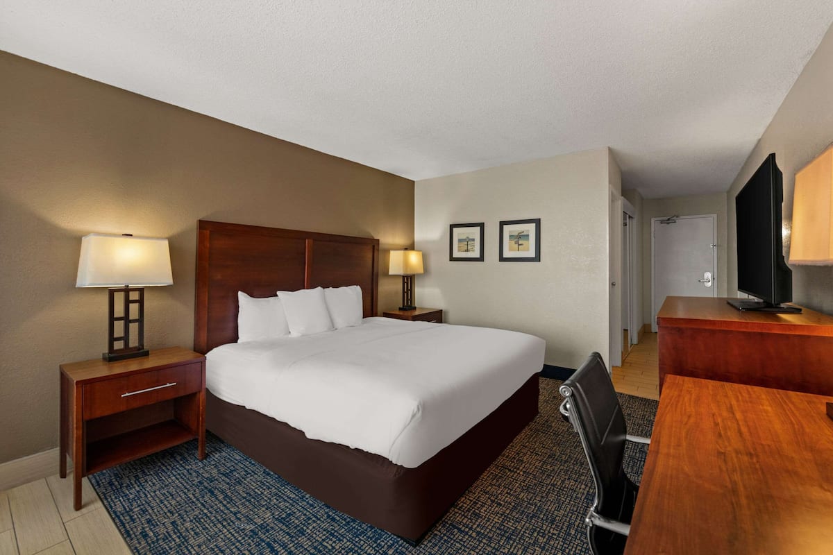 A hotel room with a large bed, two bedside lamps, a desk with a chair, and a television.