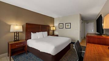 A hotel room with a large bed, two bedside lamps, a desk with a chair, and a television.