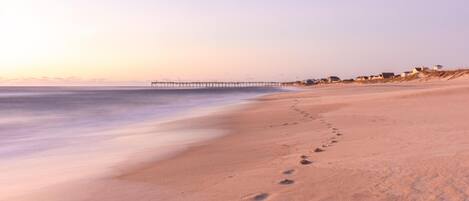 A beach with footprints leading to a pier.