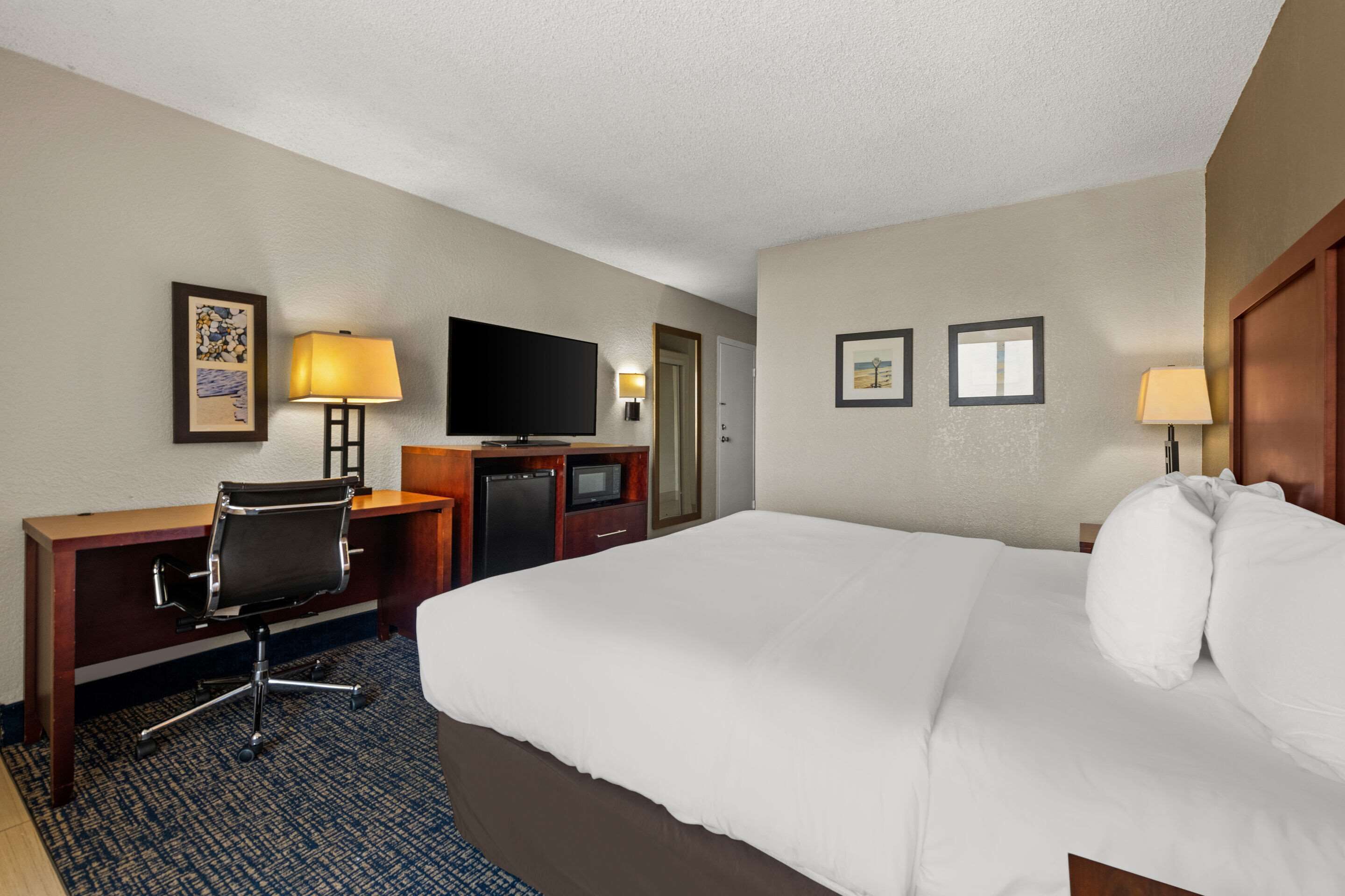 A hotel room with a large bed, a desk with a chair, a television, and two wall-mounted lamps.