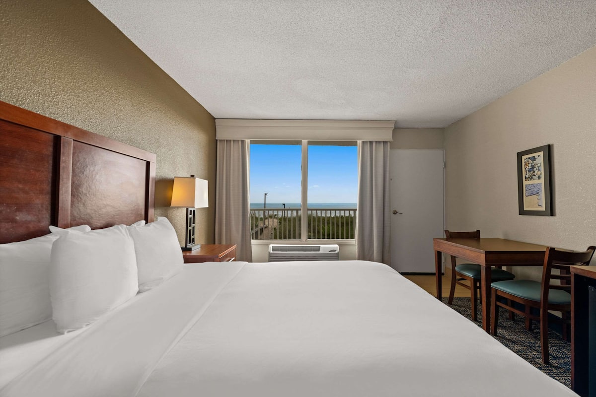A hotel room with a large bed, a desk, and a view of the beach.