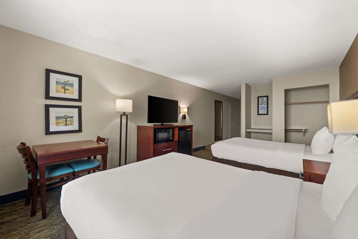 A hotel room with two beds, a desk with a chair, a television, and a microwave.