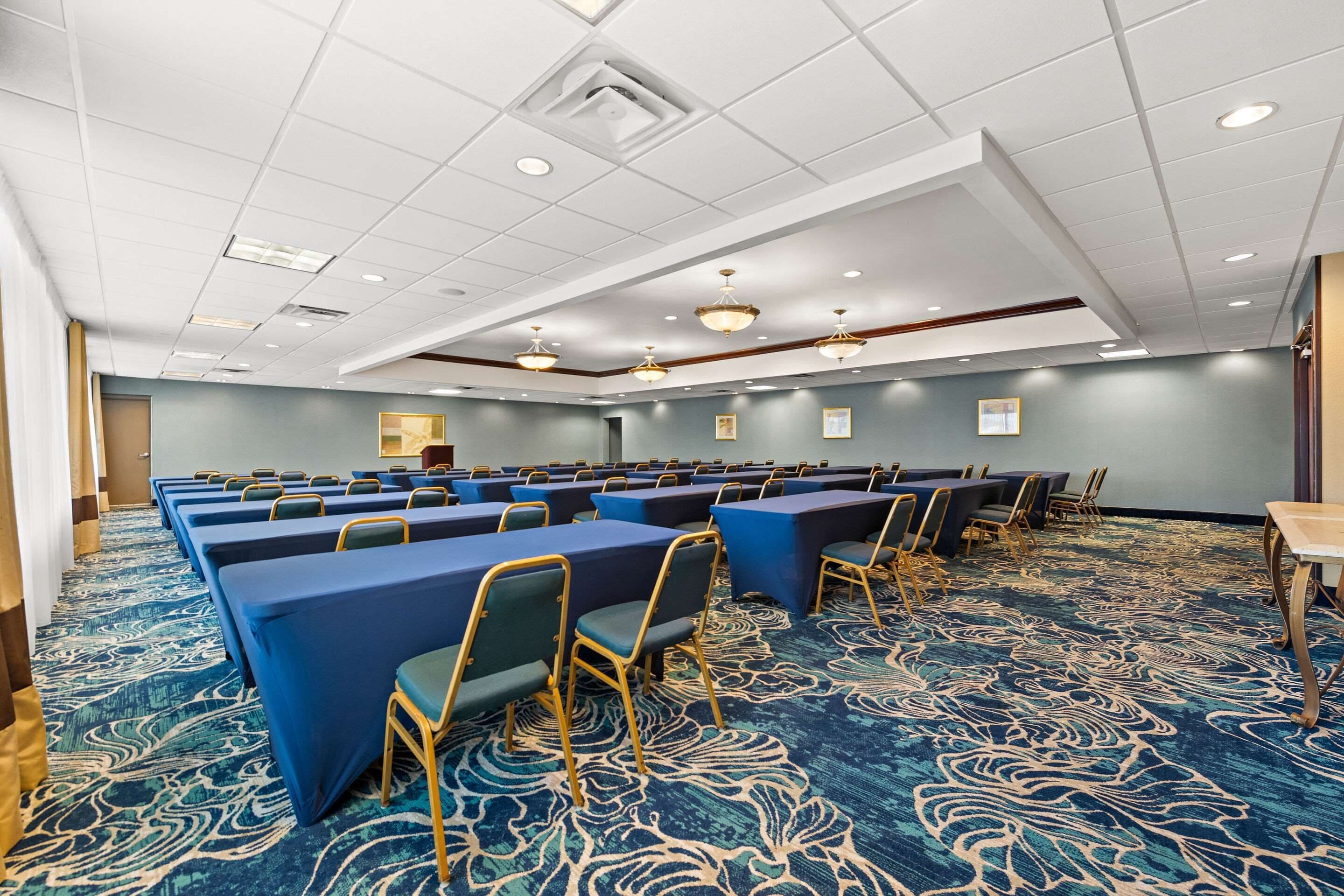 A conference room with rows of tables and chairs, a patterned carpet, and ceiling lights.