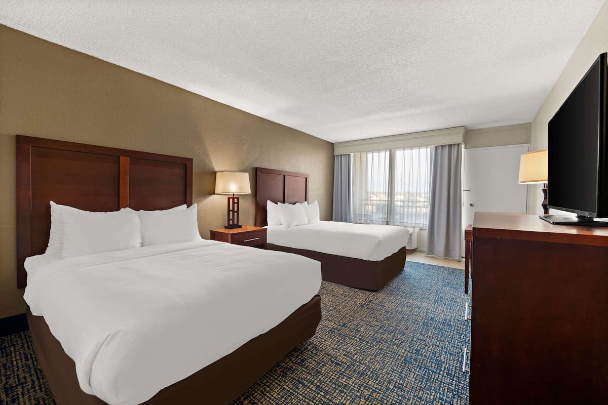 A hotel room with two large beds, a desk, a TV, and a window with curtains.