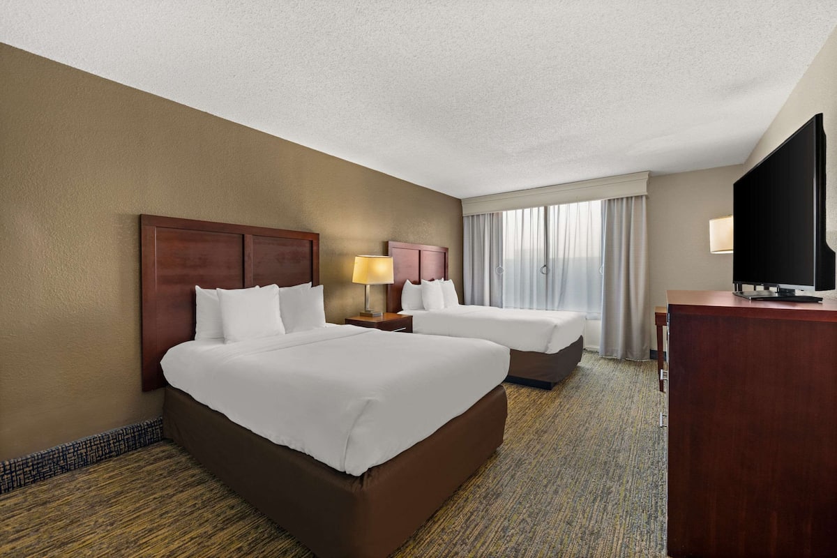 A hotel room with two beds, a desk, a TV, and a window with curtains.