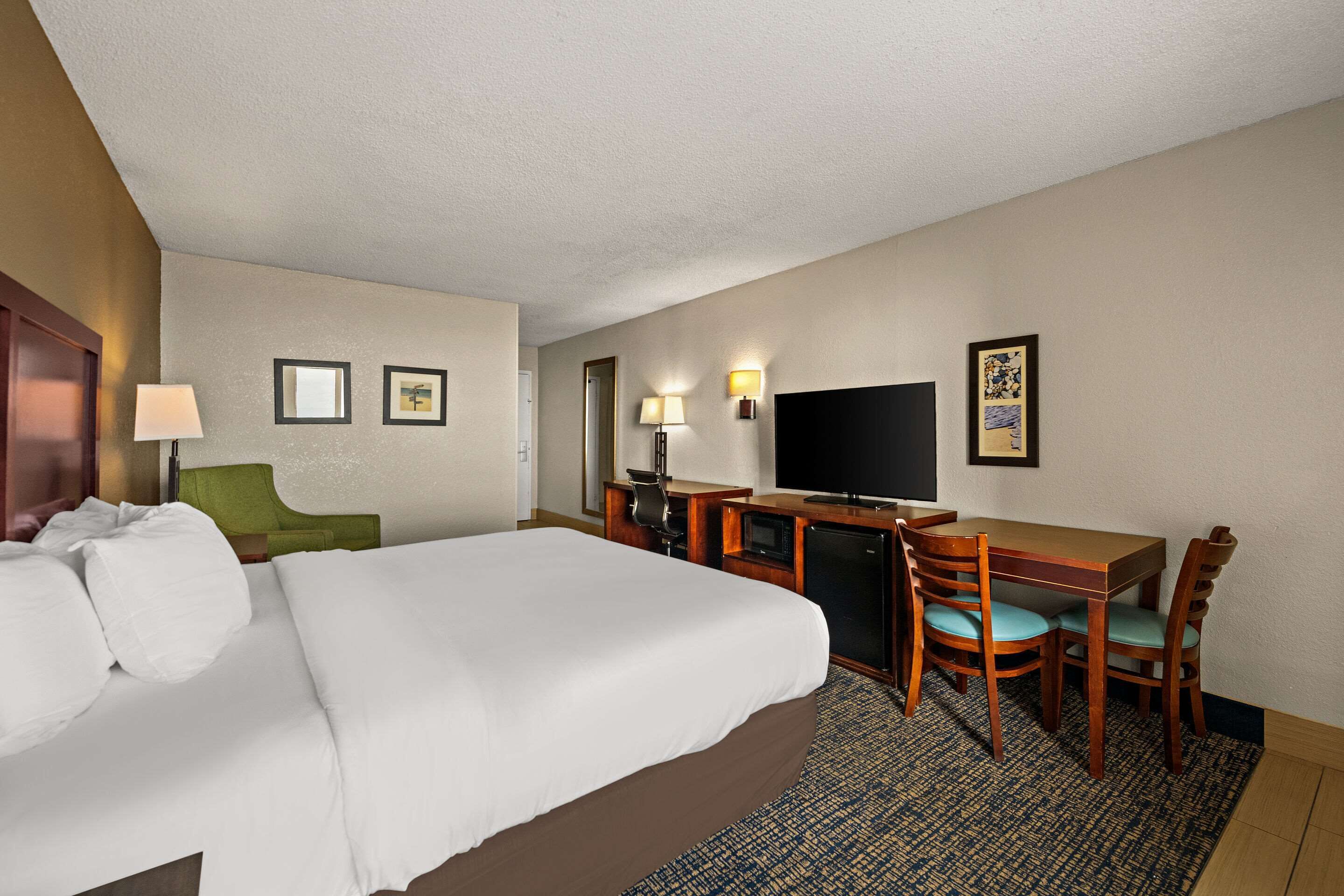 Ein Hotelzimmer mit einem großen Bett, einem Schreibtisch mit Stuhl, einem Fernseher und einem kleinen Tisch.