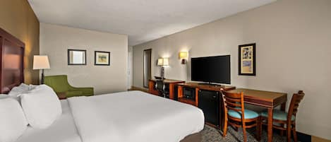 Ein Hotelzimmer mit einem großen Bett, einem Schreibtisch mit Stuhl, einem Fernseher und einem kleinen Tisch.