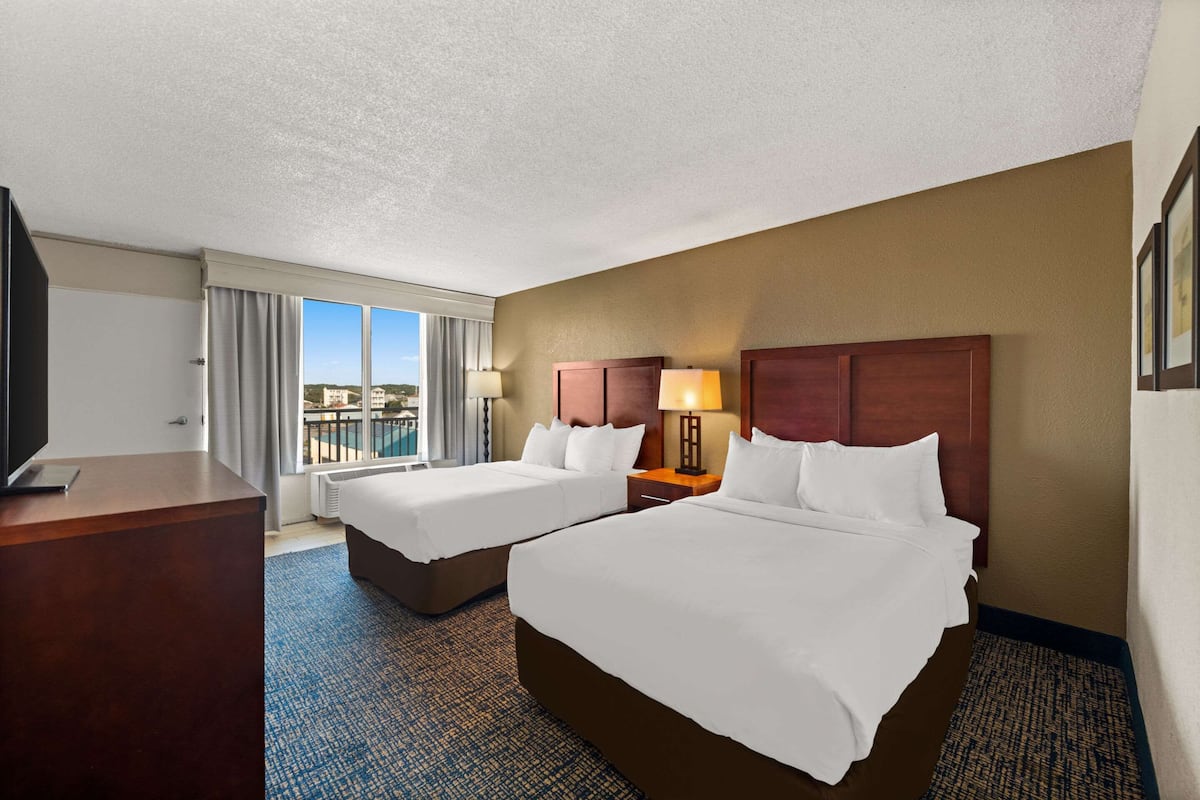 A hotel room with two beds, a desk, a TV, and a view of the city.