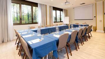 A conference room with a long table, chairs, a projector screen, and windows with curtains.
