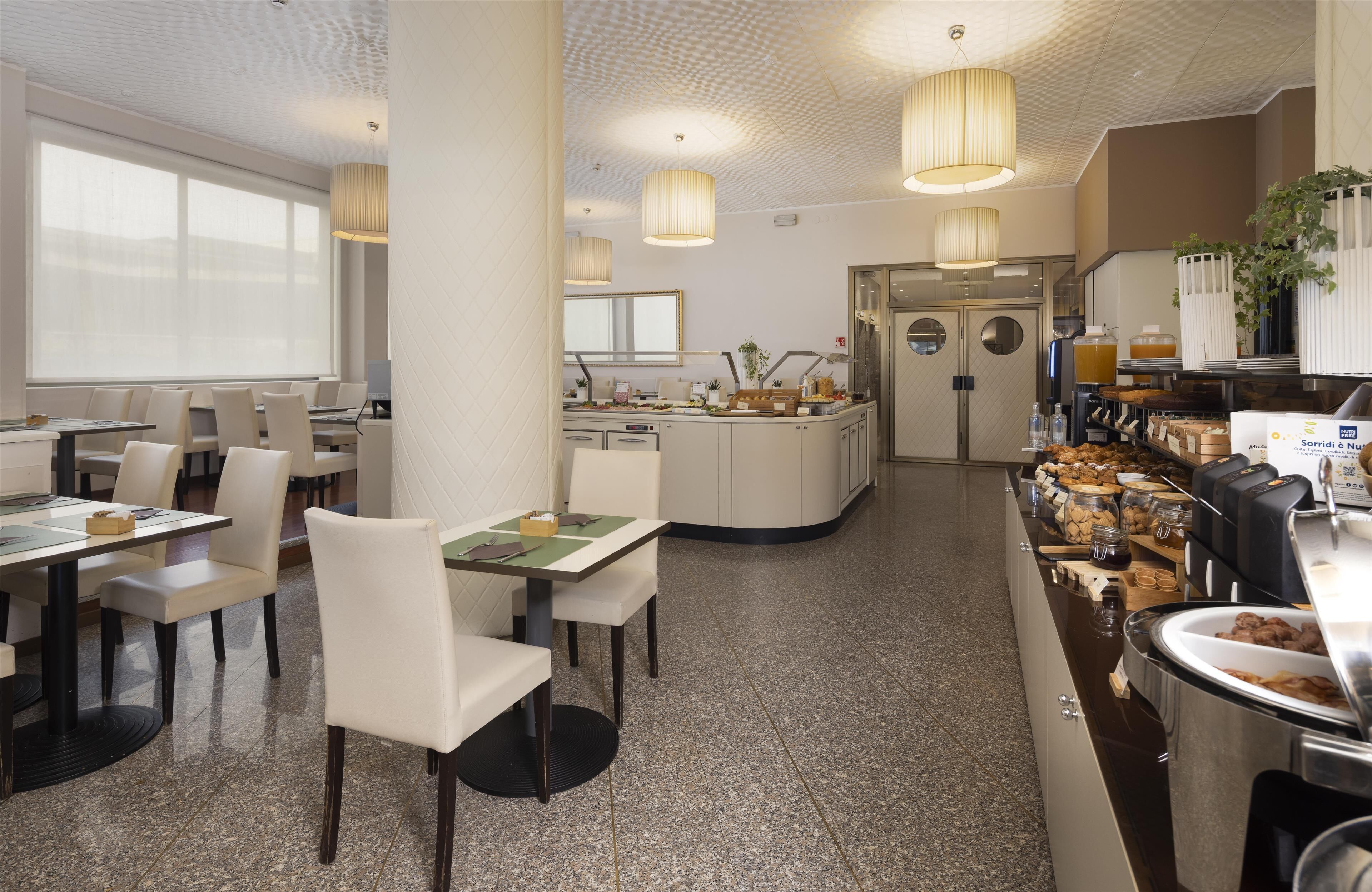 A modern dining area with white chairs and tables, a buffet with various food items, and a clean, tiled floor.