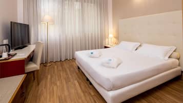 Una camera d'albergo con un letto, una scrivania con televisore, una sedia, una lampada e un comodino.