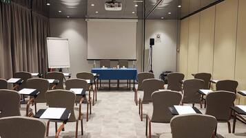 Un salón de conferencias con filas de sillas, una pantalla de proyector y una pizarra.
