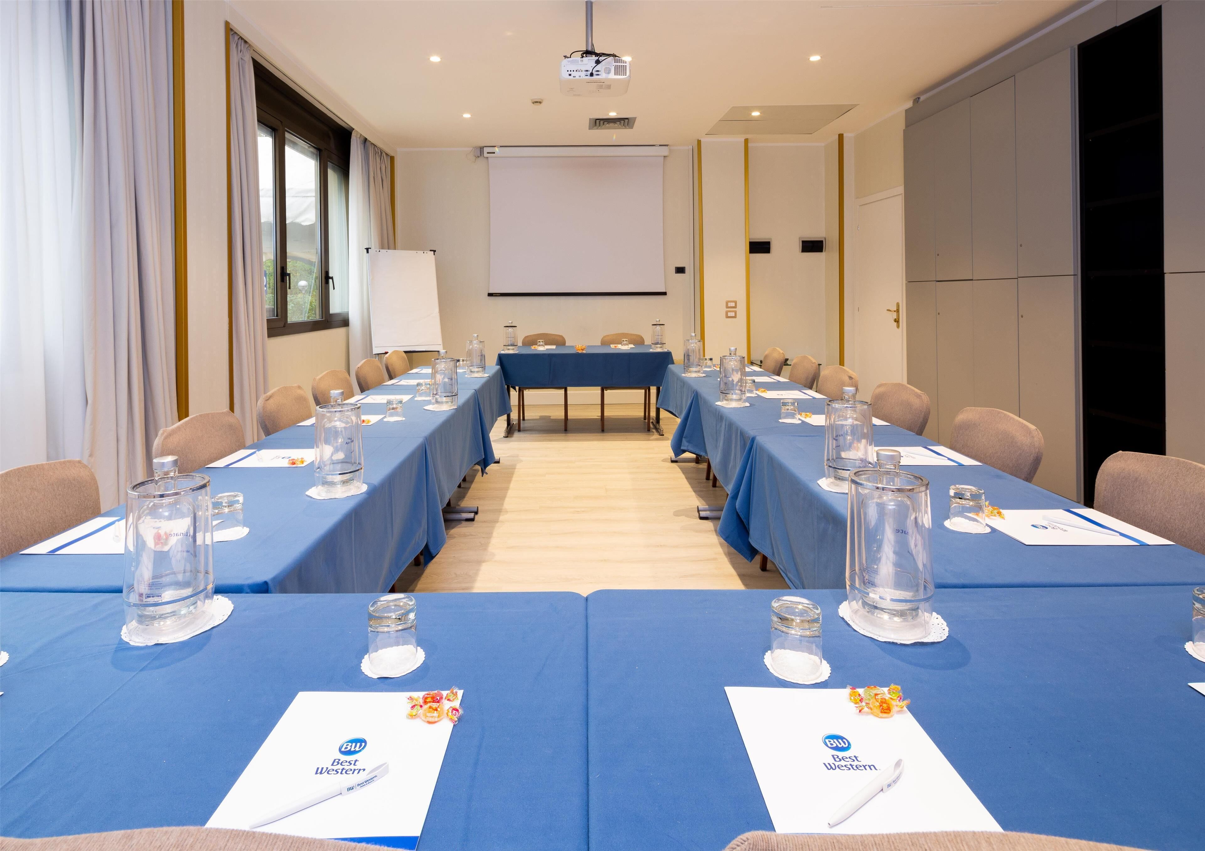 A conference room with long tables, chairs, and a projector screen.