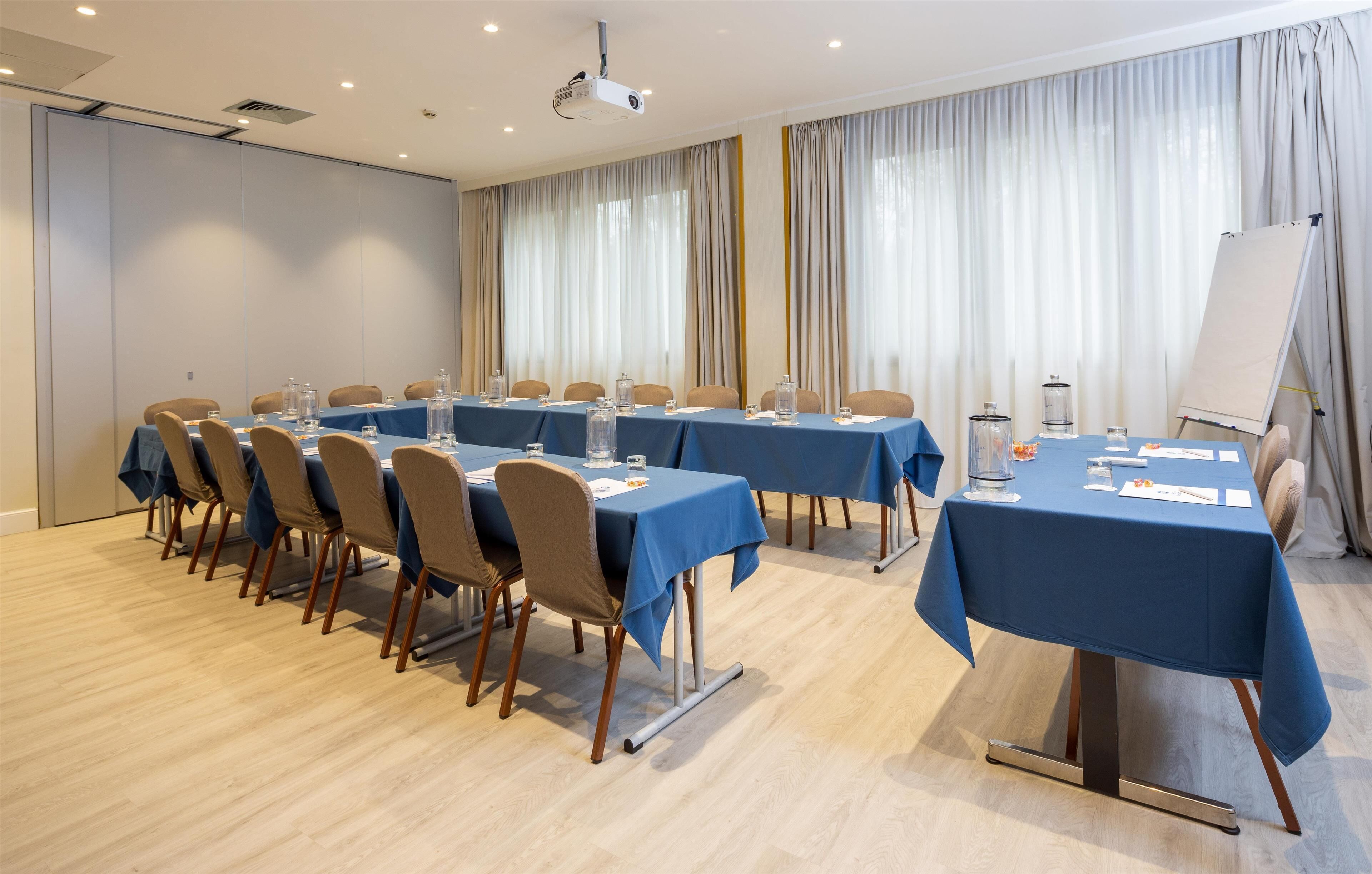 Een vergaderzaal met meerdere tafels, stoelen, een beamer en een whiteboard.