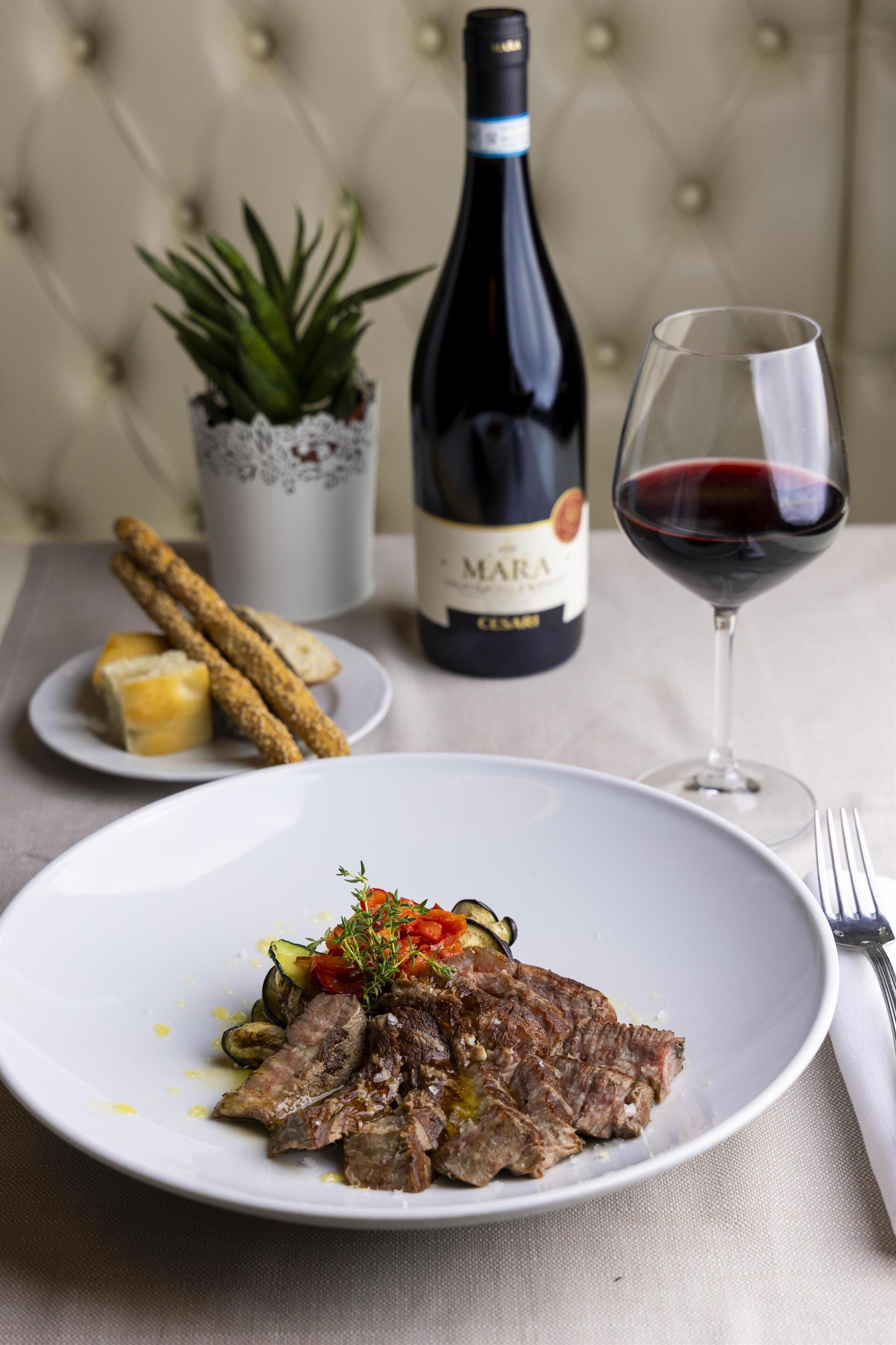 A dining table with a plate of food, a bottle of wine, and a glass of wine.