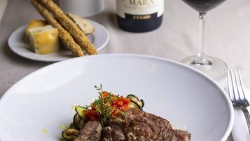 A dining table with a plate of food, a bottle of wine, and a glass of wine.