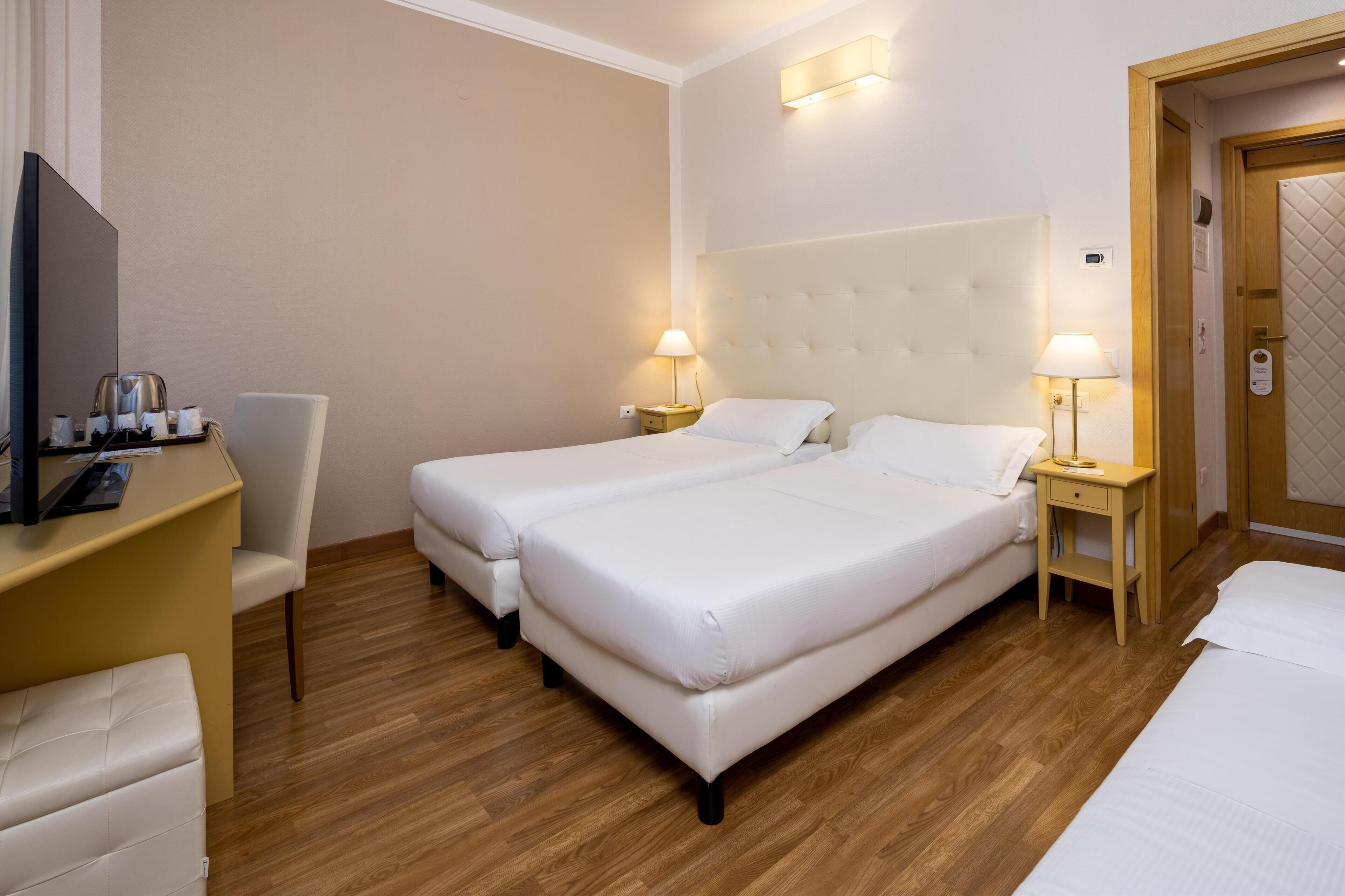 Een hotelkamer met twee bedden, een bureau met een televisie en bedlampjes.