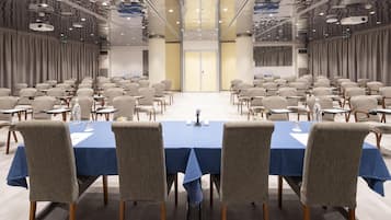 Un salón de conferencias con filas de mesas y sillas, un mantel azul y un diseño moderno en el techo.
