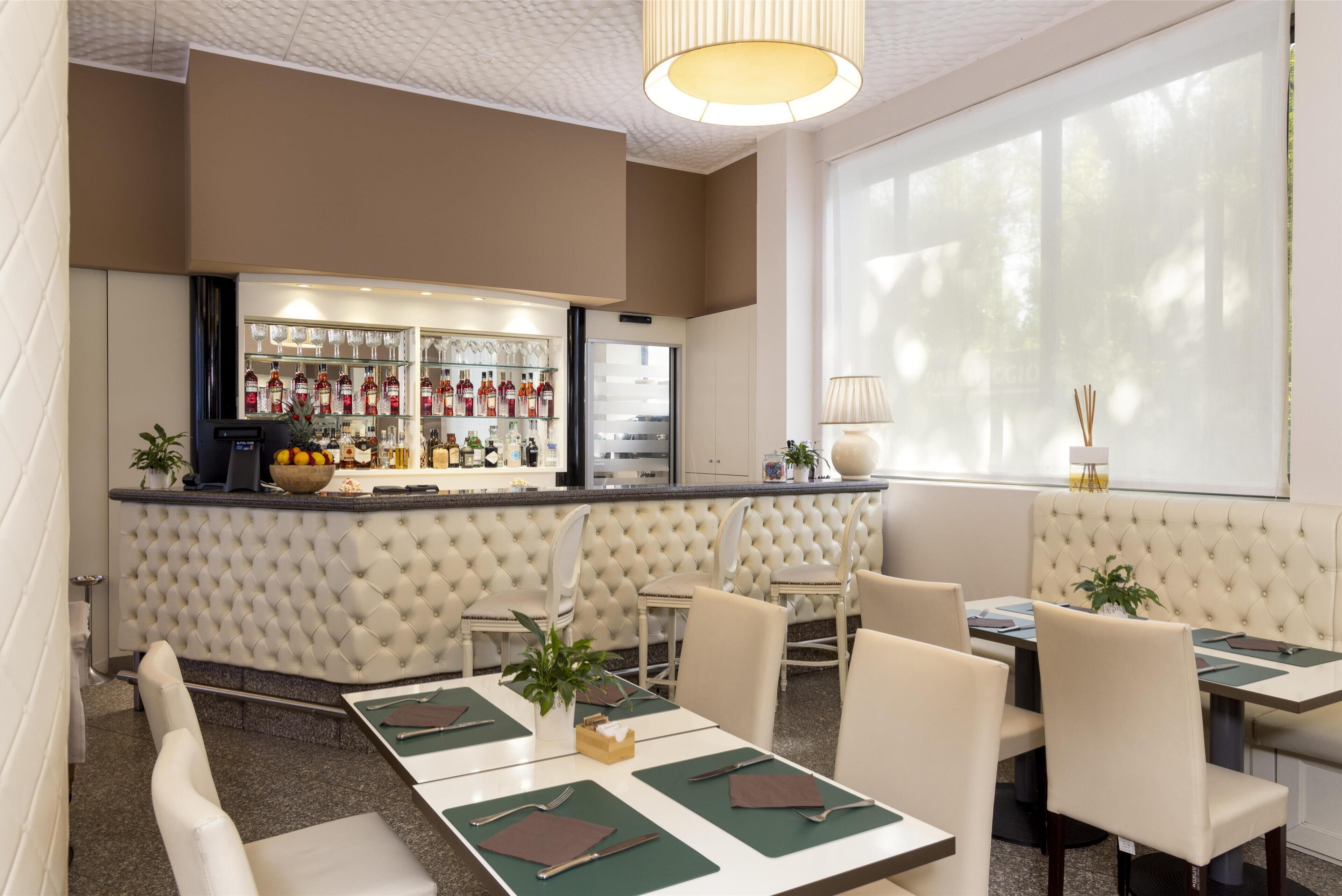 Un restaurante con zona de bar, asientos acolchados y vistas a árboles a través de amplios ventanales.