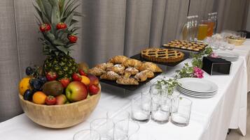 Una mesa de buffet con frutero, pastelería y vasos.