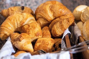 Una cesta llena de diferentes tipos de pan, incluyendo croissants y barras.