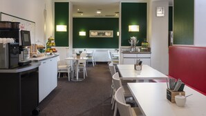 A modern restaurant with white tables and chairs, a counter with a coffee machine, and green walls. - Wyndham Garden Düsseldorf City Centre Königsallee (Düsseldorf)