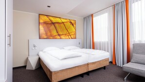 A modern hotel room with a double bed, a grey armchair, and a large abstract painting on the wall. - Wyndham Garden Düsseldorf City Centre Königsallee (Düsseldorf)