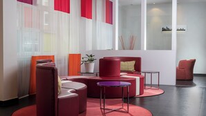 A modern lounge area with red and white furnishings, a small table, and a potted plant. - Wyndham Garden Düsseldorf City Centre Königsallee (Düsseldorf)
