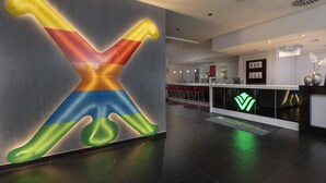 A modern hotel lobby with a large, illuminated wall art piece and a reception desk with a green logo. - Wyndham Garden Düsseldorf City Centre Königsallee (Düsseldorf)