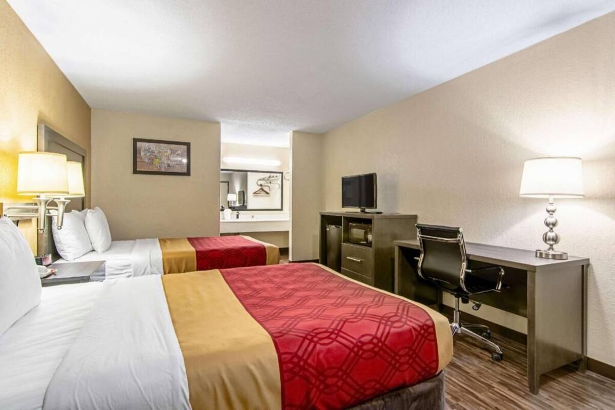 A hotel room with two beds, a desk, a chair, a TV, and a lamp.