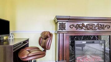 A room with a leather chair, a television, a fireplace, and a marble fireplace surround.