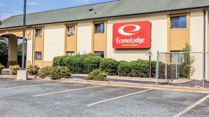 Edificio di EconoLodge Inn & Suites a due piani con logo rosso, parcheggio e recinzione in rete metallica.