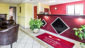 Un'area reception con arredamento rosso e giallo, una scrivania della reception, un orologio e una pianta in vaso.