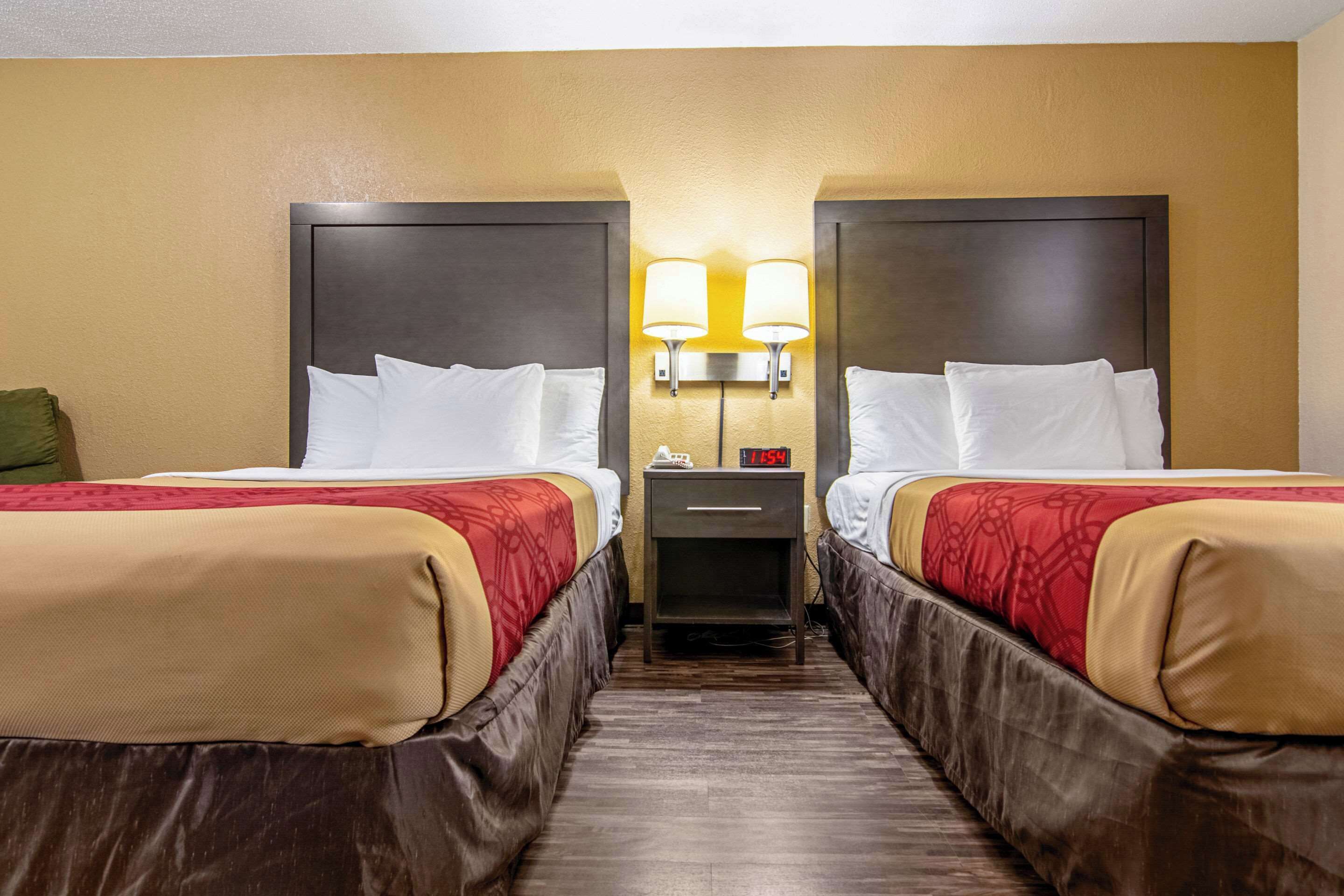 Ein Hotelzimmer mit zwei Betten, jeweils mit Kopfteil, Nachttisch und Lampe sowie einer Uhr.