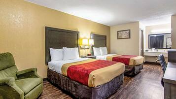 A hotel room with two beds, a green armchair, a desk, and a mirror.