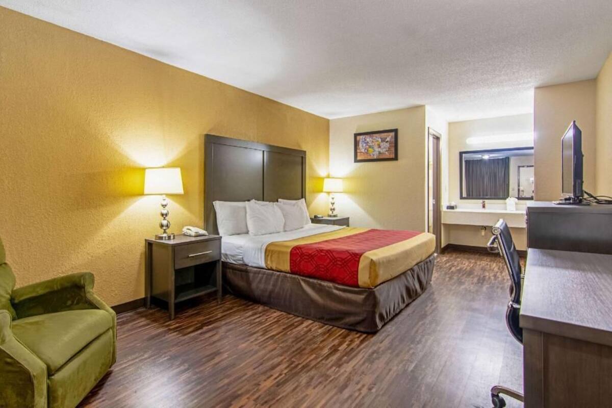A hotel room with a bed, bedside tables, a desk, a chair, and a television.