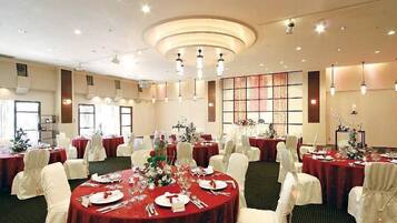 A banquet hall with round tables set for dining, white chairs, and a central decorative wall.