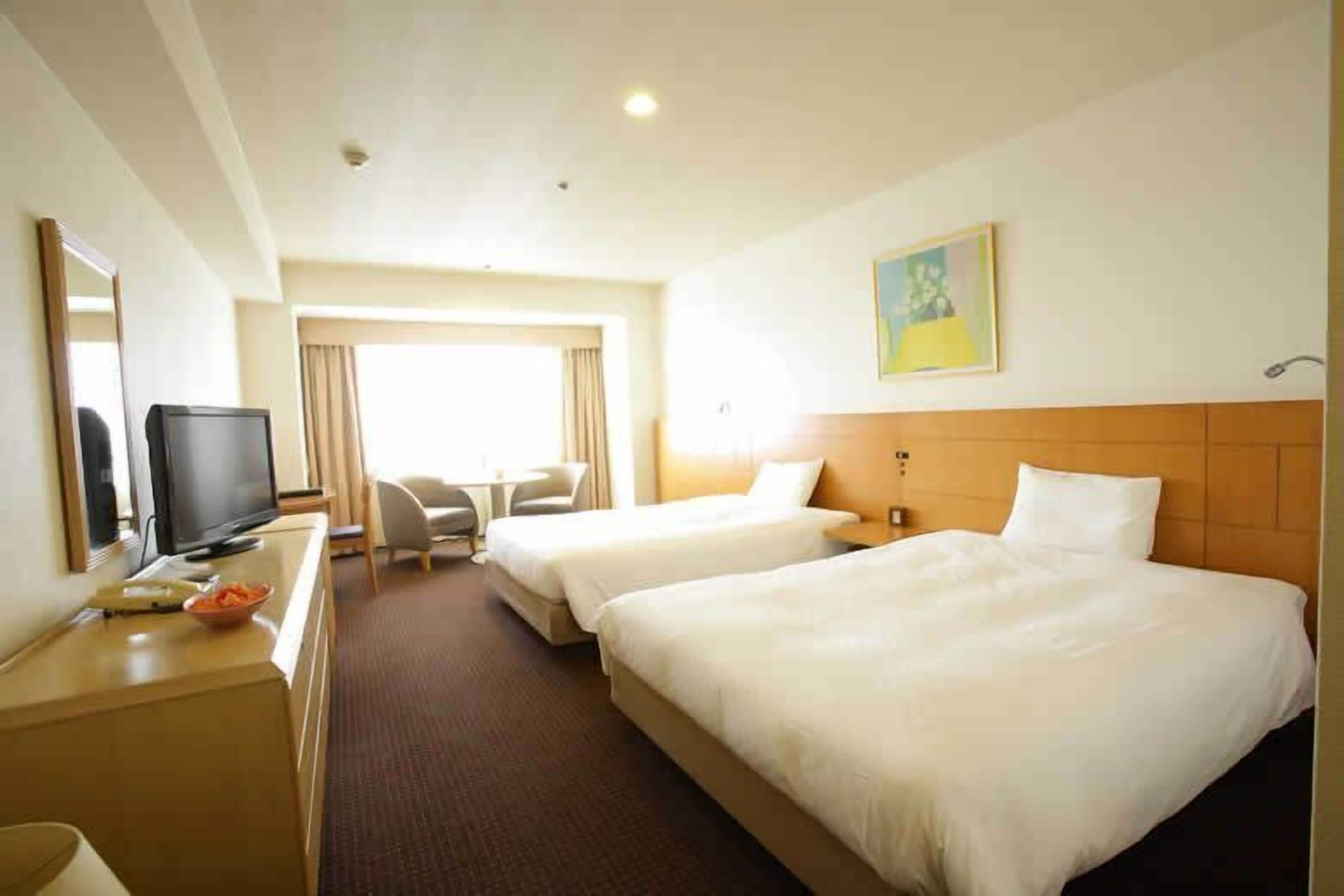 A hotel room with two beds, a desk with a television, a chair, and a painting on the wall.