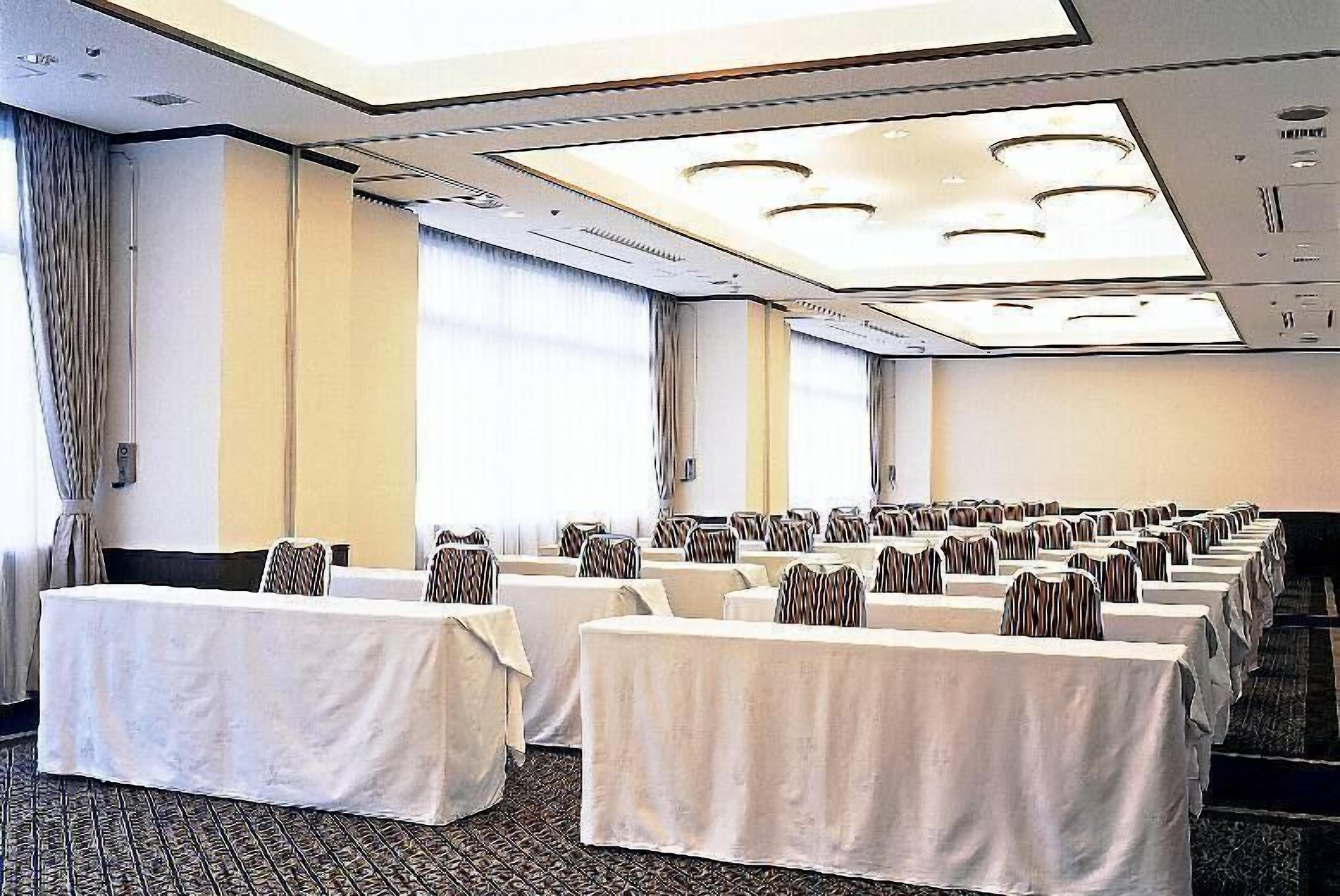 A conference room with rows of tables, each covered with a white tablecloth and striped chairs.