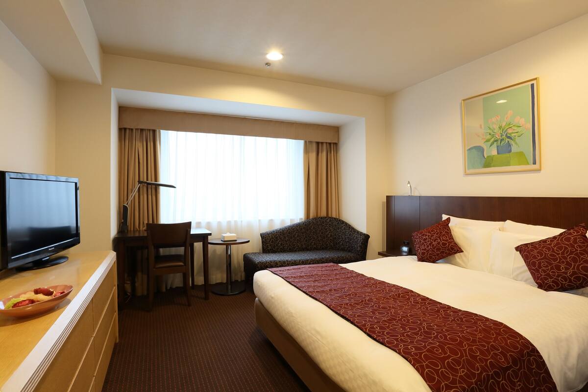 Habitación de hotel con una cama grande, televisión, escritorio con silla y ventana con cortinas.