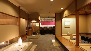 Een traditionele Japanse lobby met tatami vloermatten, houten balken en een receptiebalie.