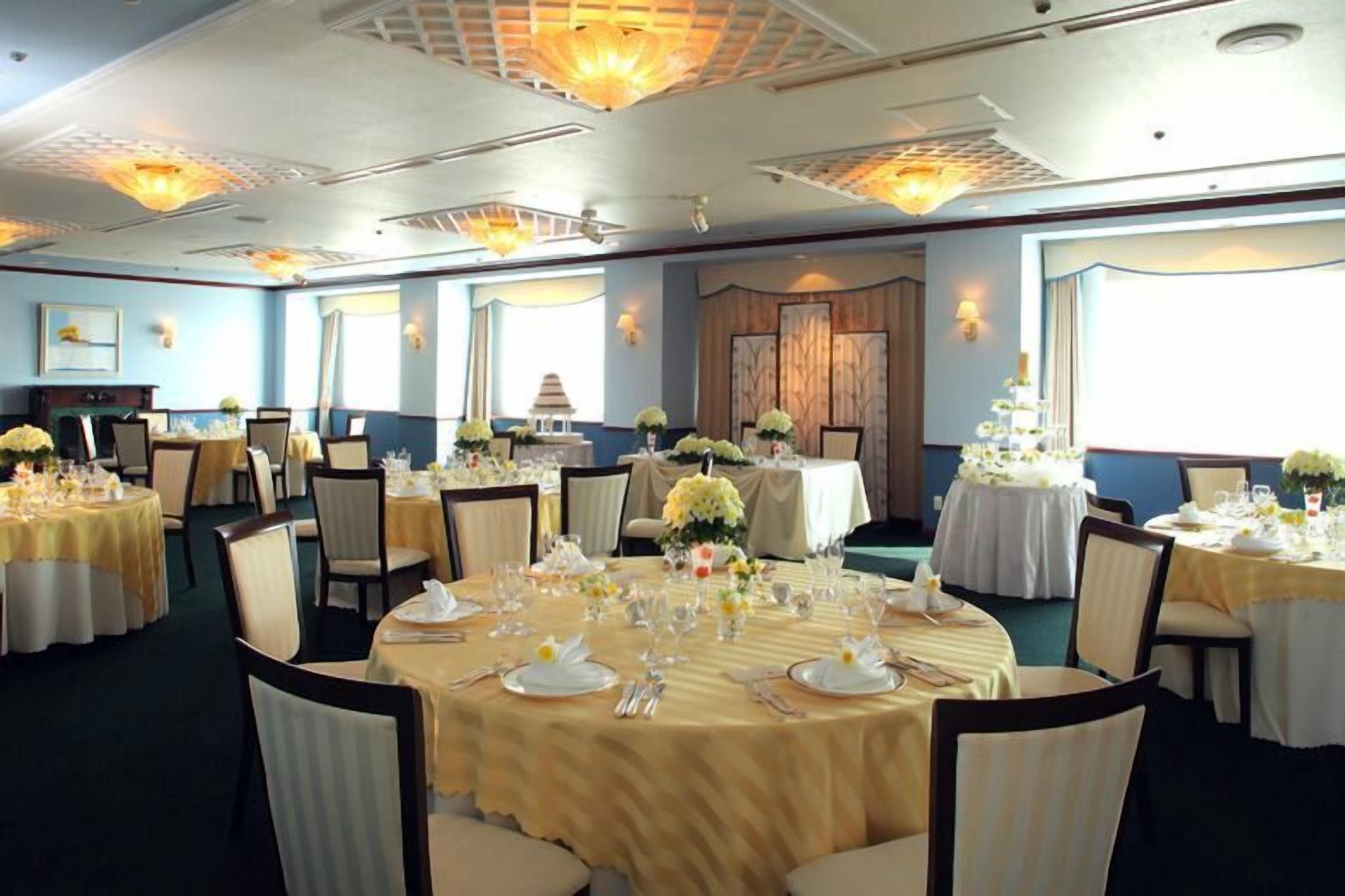 A banquet hall with round tables set for a formal event, featuring floral centerpieces and white tablecloths.