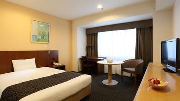 A hotel room with a large bed, a desk with a television, a small table, and a chair.