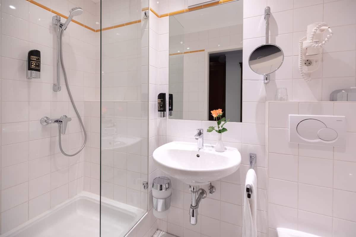 Une salle de bain moderne avec une douche à parois de verre, un lavabo blanc et une douchette à main.