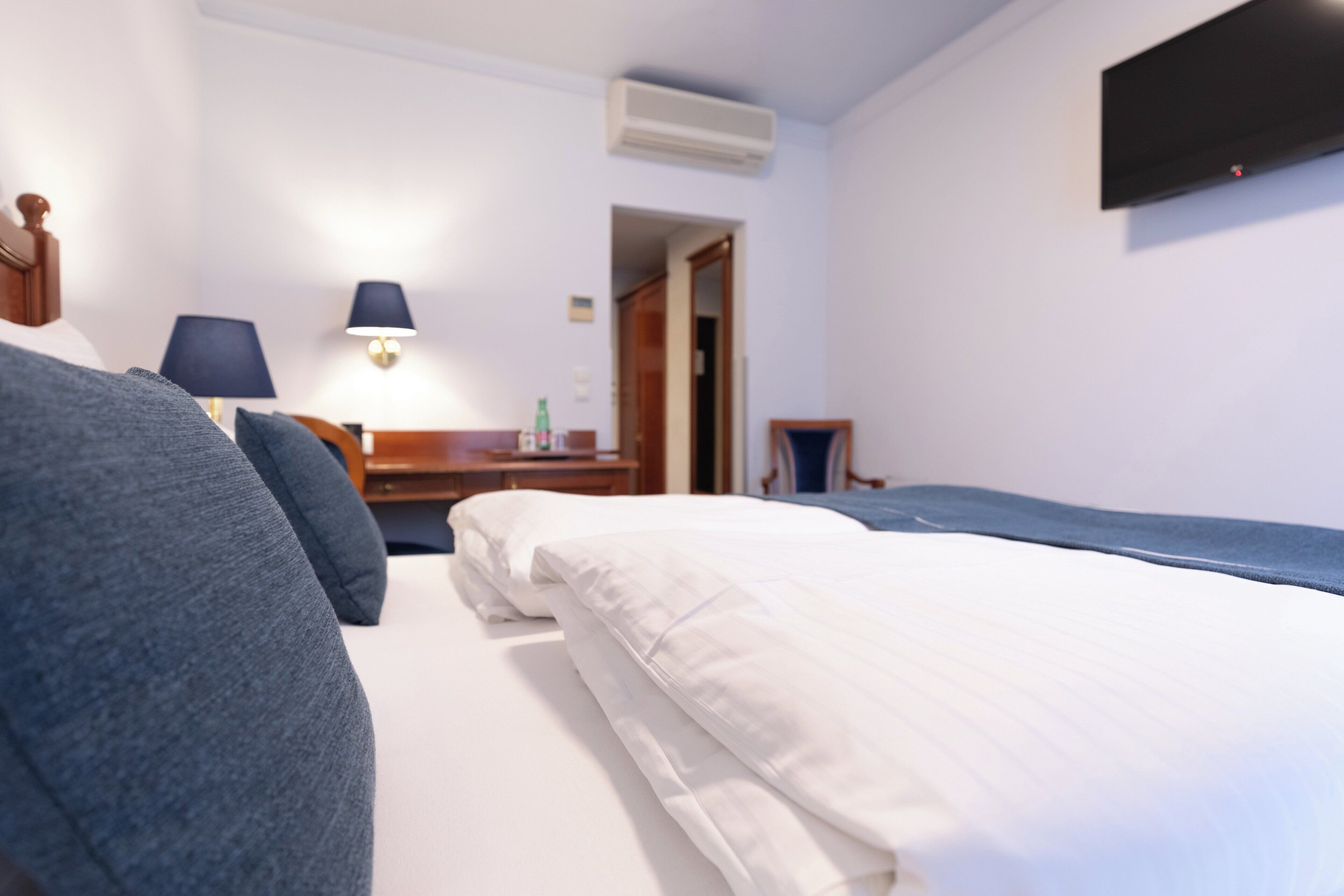 Une chambre d’hôtel comprenant un lit, un bureau avec une lampe, un téléviseur fixé au mur et un appareil de climatisation.