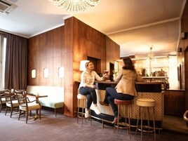 Angolo bar con rivestimenti in legno, bancone, sgabelli e una zona salotto con poltrone.