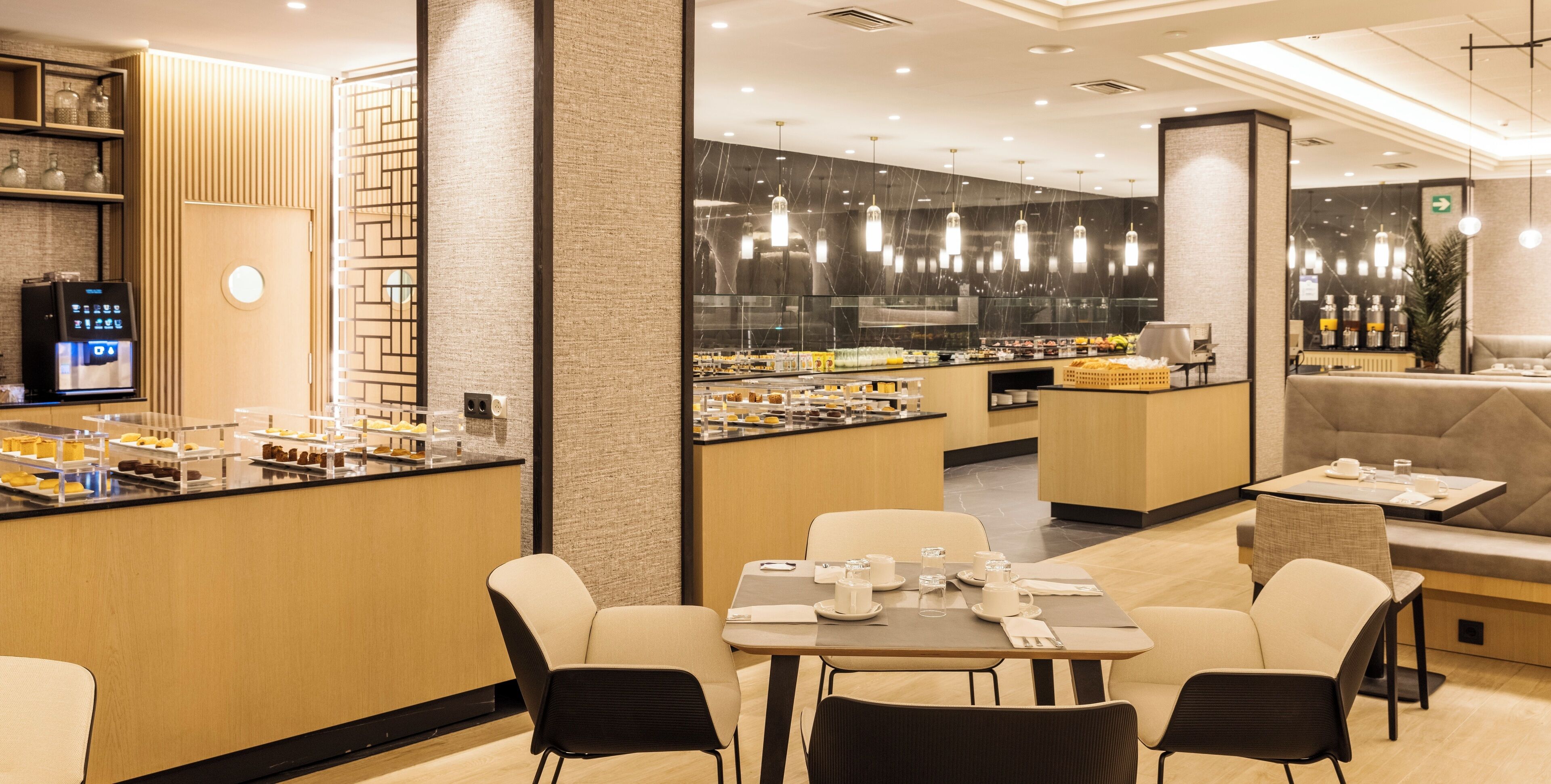 A modern restaurant with a counter displaying various food items, a seating area with tables and chairs, and a large mirror on the wall.